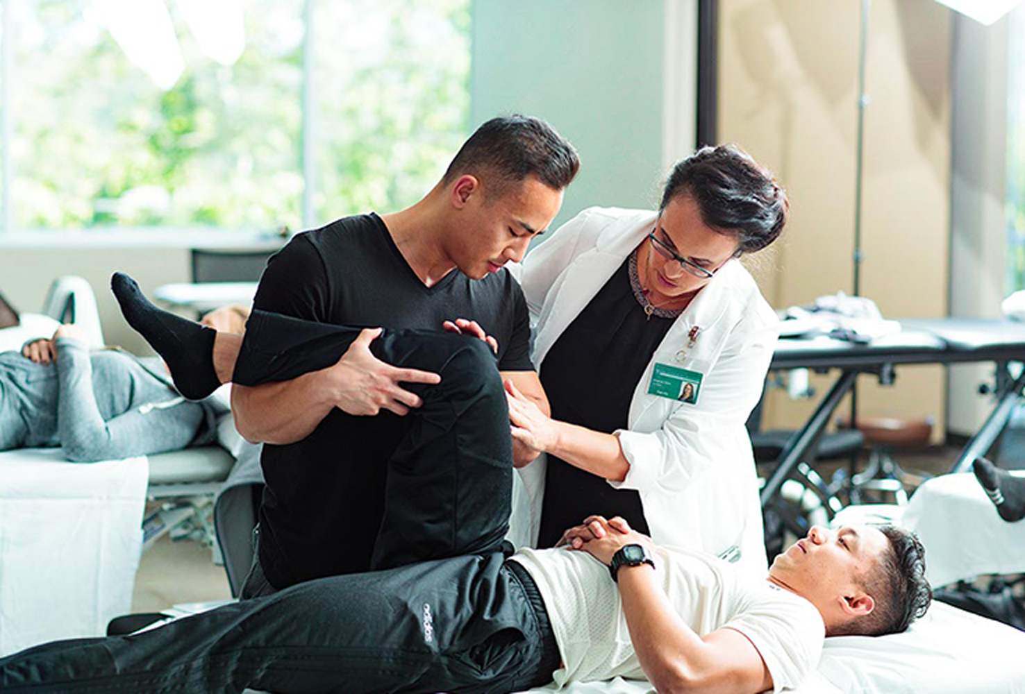 Two physical therapists standing over patient bending leg to assess movement.