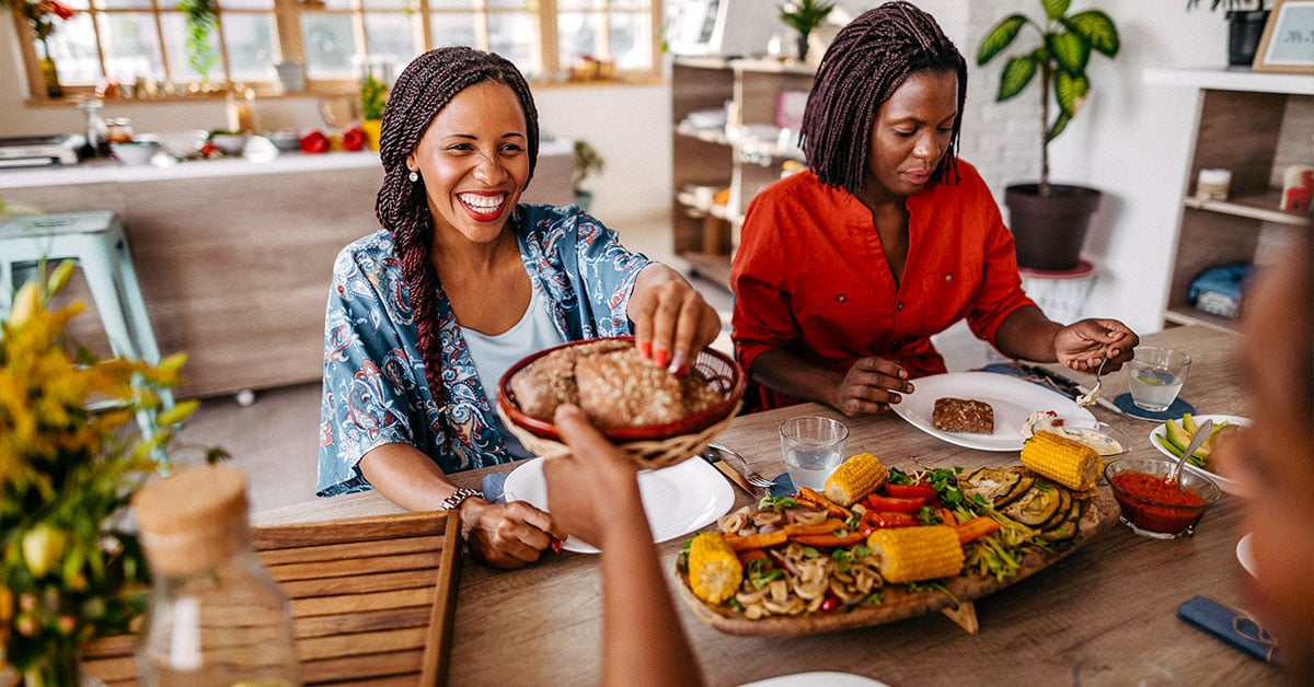 two women enjoying a plant-based meal of corn and vegetables