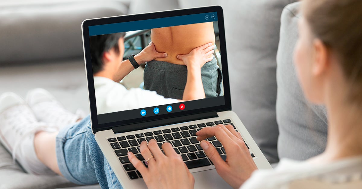 A woman on her laptop looks at an image of a physical therapist massaging a patient’s lower back.