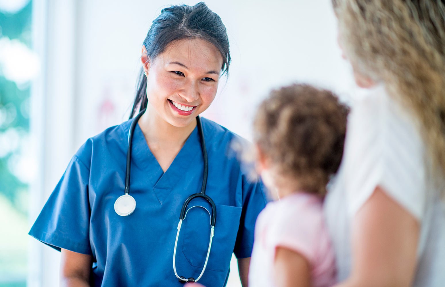 Female API nurse smiles looking at young female child in foreground